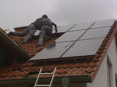 Bild vergrößern: zu sehen sind zwei Handwerker, die auf dem Dach Solarmodule anbringen